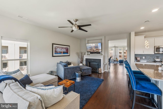 living room with visible vents, ceiling fan, recessed lighting, a glass covered fireplace, and dark wood-style flooring