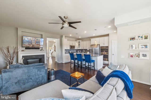 living room with dark wood-type flooring, baseboards, recessed lighting, a fireplace, and a ceiling fan