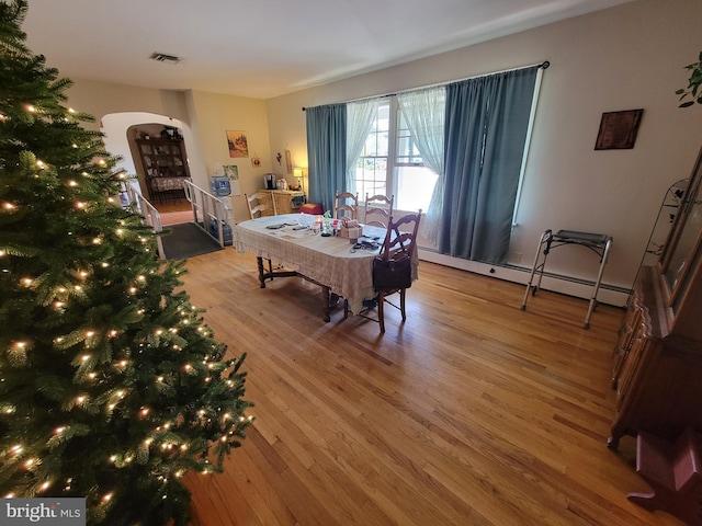 dining room with visible vents, stairs, wood finished floors, arched walkways, and a baseboard radiator