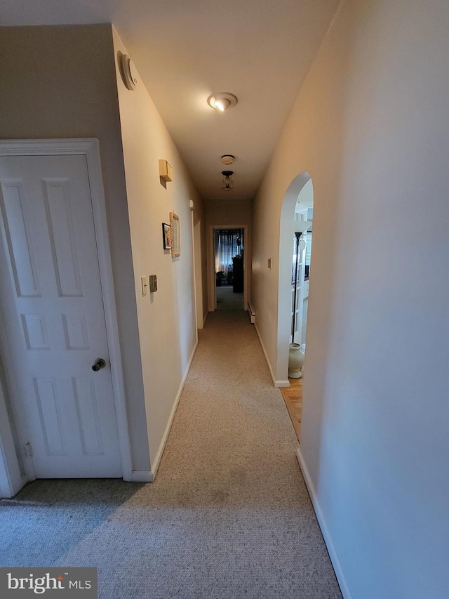 hall featuring baseboards, arched walkways, and light carpet