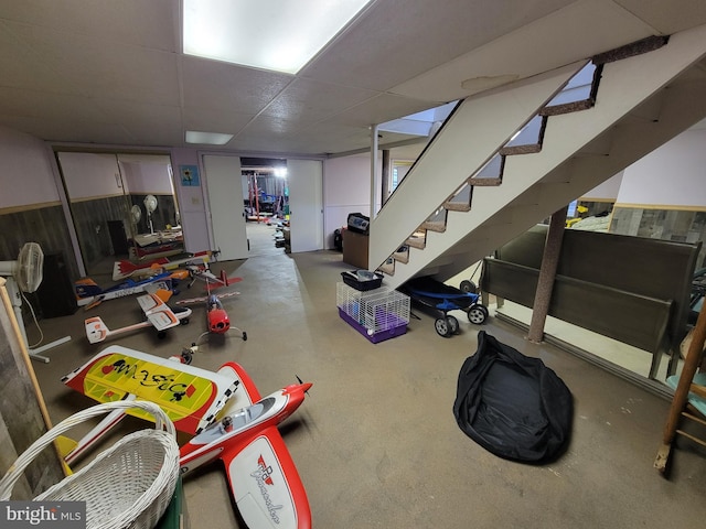 finished below grade area featuring a drop ceiling, a wainscoted wall, and stairway