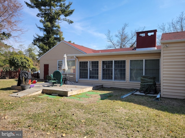 rear view of house with a deck, a lawn, fence, and a chimney