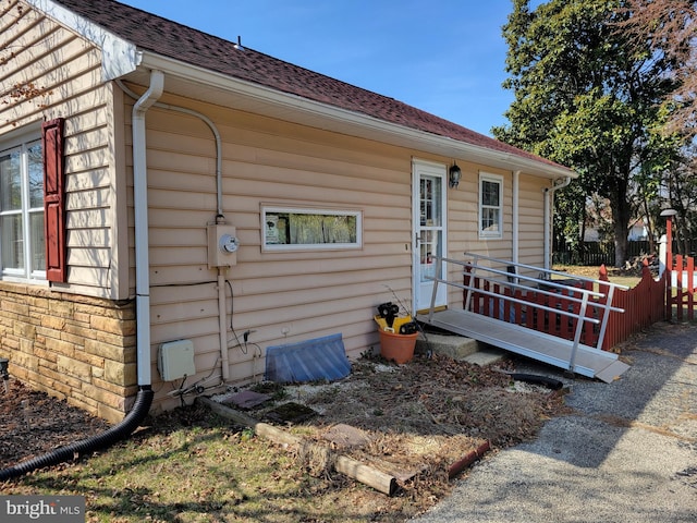 view of side of home with stone siding, a shingled roof, and fence