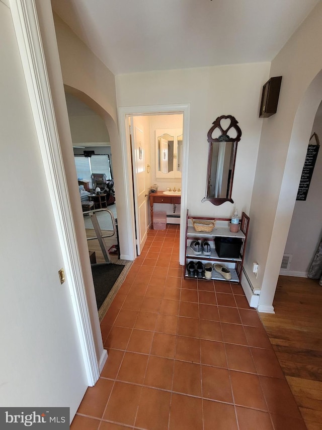 hall featuring tile patterned flooring, visible vents, arched walkways, and a baseboard radiator