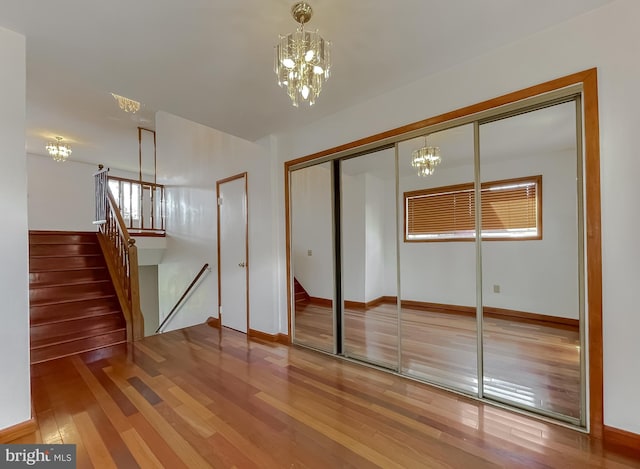 unfurnished bedroom featuring hardwood / wood-style floors, an inviting chandelier, baseboards, and a closet