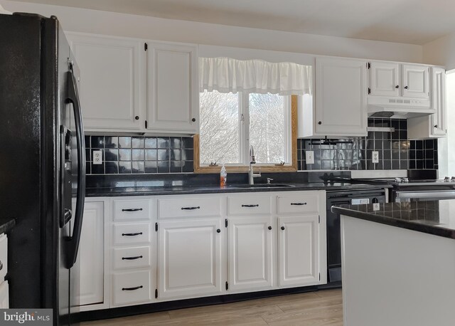 kitchen featuring white cabinetry, freestanding refrigerator, a sink, under cabinet range hood, and dishwasher