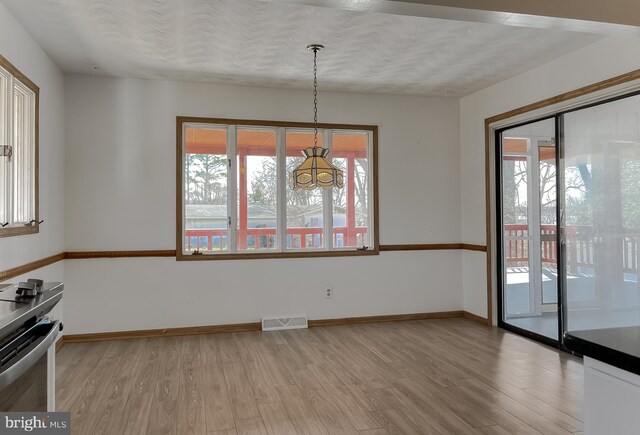 unfurnished dining area featuring light wood finished floors, visible vents, a textured ceiling, and baseboards