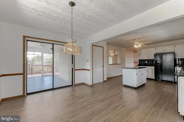 kitchen with wood finished floors, white cabinetry, dark countertops, tasteful backsplash, and black fridge