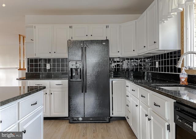 kitchen with tasteful backsplash, light wood-style flooring, white cabinets, black appliances, and a sink