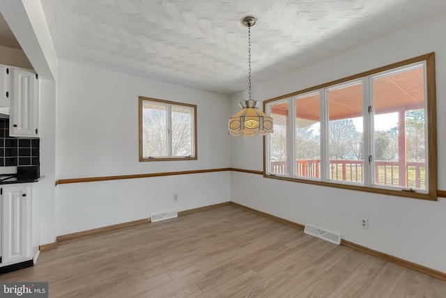 unfurnished dining area featuring visible vents, light wood-type flooring, and baseboards