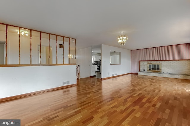 unfurnished living room featuring light wood-type flooring, visible vents, an inviting chandelier, and a fireplace