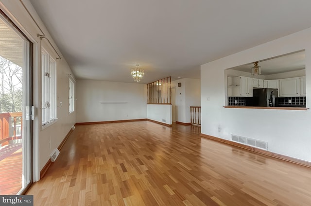 unfurnished living room featuring a notable chandelier, visible vents, and light wood-style floors