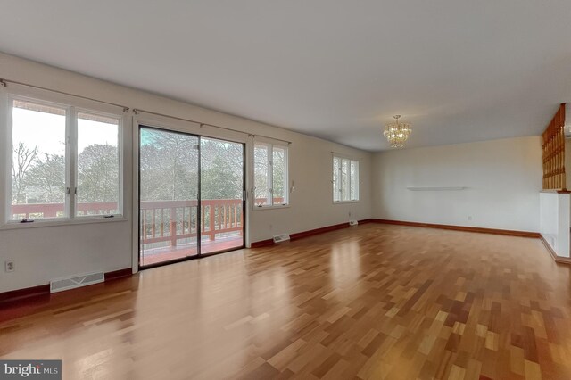 unfurnished living room with visible vents, baseboards, light wood-style floors, and an inviting chandelier