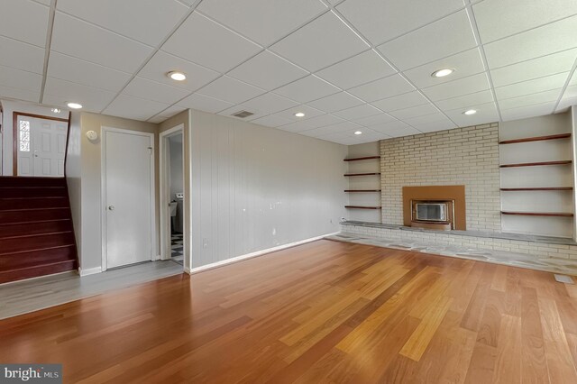 unfurnished living room featuring baseboards, built in shelves, a brick fireplace, and wood finished floors