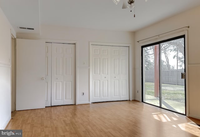 unfurnished bedroom featuring multiple windows, multiple closets, access to exterior, and light wood finished floors