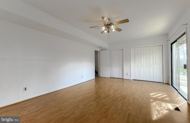 unfurnished bedroom with two closets, ceiling fan, and wood finished floors