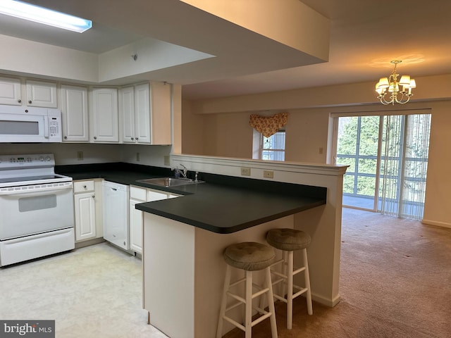 kitchen featuring dark countertops, a peninsula, an inviting chandelier, white appliances, and a sink