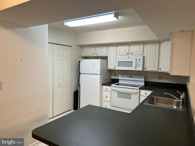 kitchen with dark countertops, a peninsula, white cabinets, white appliances, and a sink