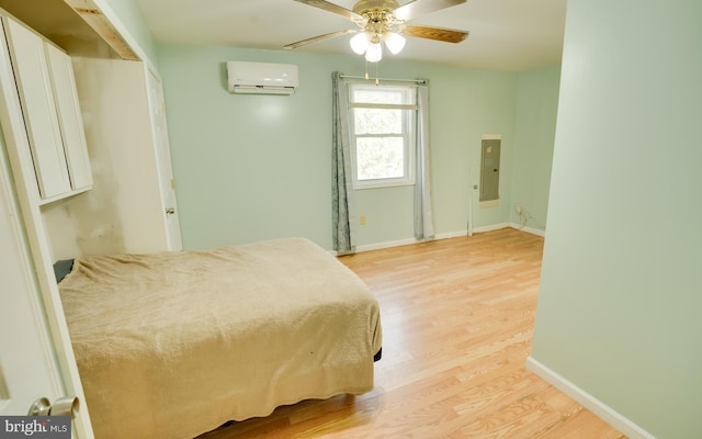 bedroom featuring electric panel, a wall mounted air conditioner, light wood-type flooring, and baseboards