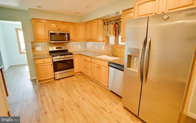 kitchen with light wood-style flooring, light brown cabinetry, a sink, backsplash, and stainless steel appliances