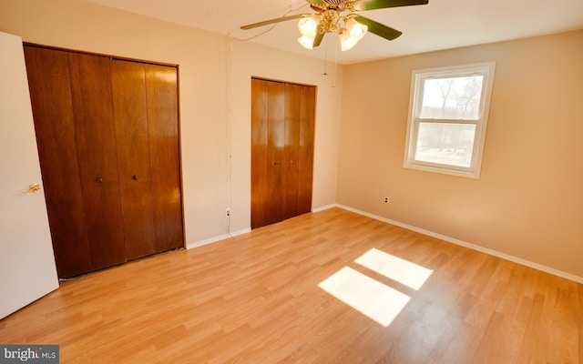 unfurnished bedroom featuring ceiling fan, wood finished floors, multiple closets, and baseboards