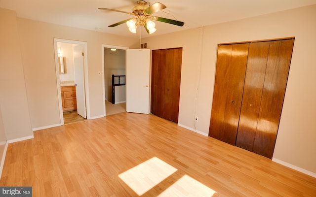 unfurnished bedroom with visible vents, multiple closets, ensuite bath, light wood finished floors, and baseboards