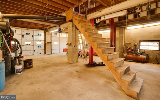 basement featuring stairs, concrete block wall, and a garage