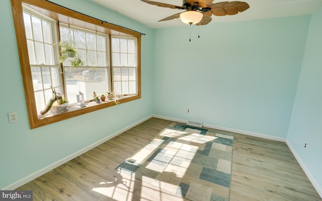 empty room featuring a ceiling fan, visible vents, wood finished floors, and baseboards