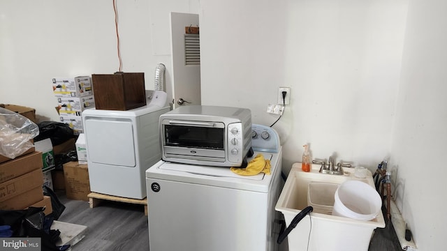 laundry room with laundry area, washing machine and dryer, a sink, and wood finished floors