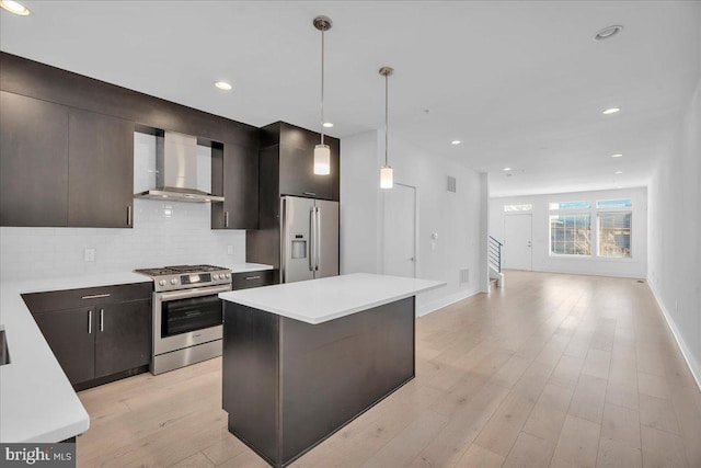 kitchen featuring wall chimney range hood, tasteful backsplash, appliances with stainless steel finishes, light wood finished floors, and light countertops