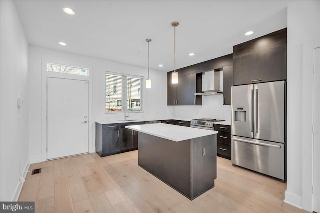 kitchen with visible vents, light wood finished floors, a sink, stainless steel appliances, and wall chimney range hood