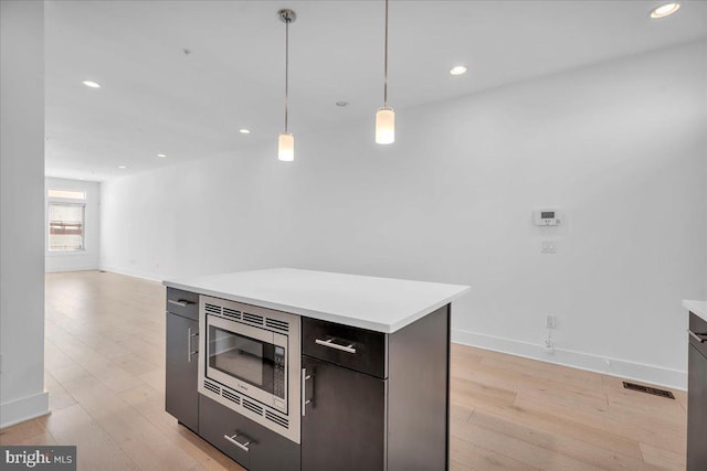 kitchen featuring visible vents, hanging light fixtures, light countertops, stainless steel microwave, and light wood-type flooring