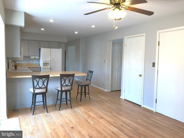 kitchen featuring gray cabinetry, light wood-style flooring, white refrigerator with ice dispenser, a peninsula, and light countertops