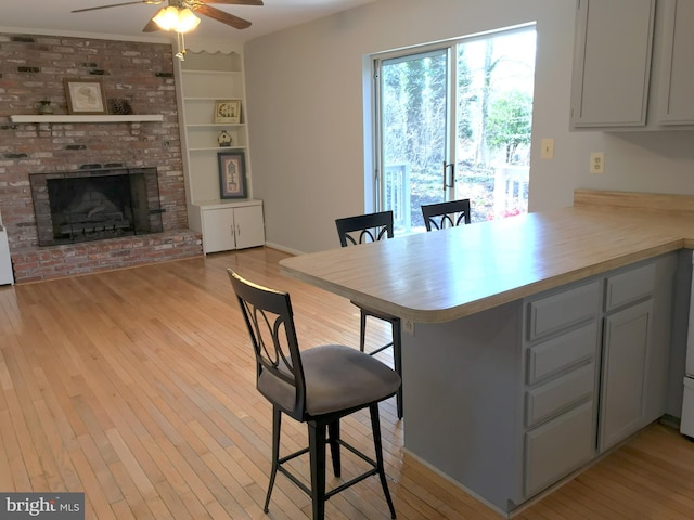 dining room featuring a brick fireplace, built in features, light wood-type flooring, and ceiling fan