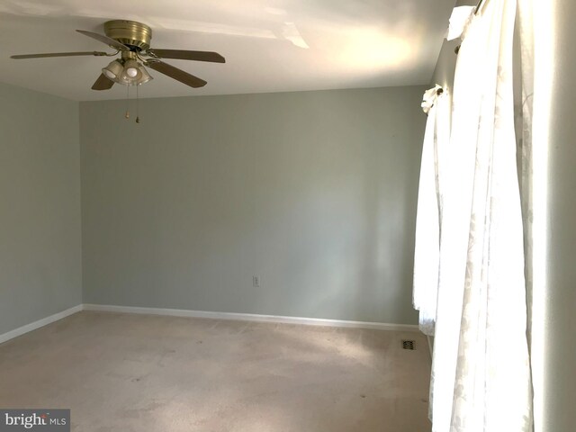 spare room featuring light colored carpet, a ceiling fan, and baseboards