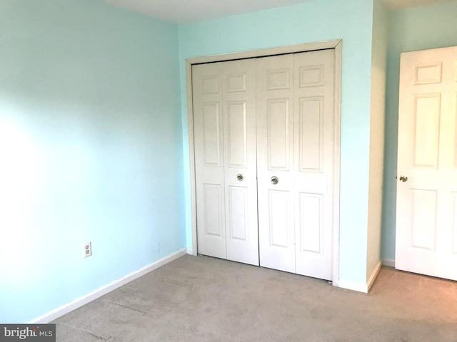 unfurnished bedroom with a closet, light colored carpet, and baseboards