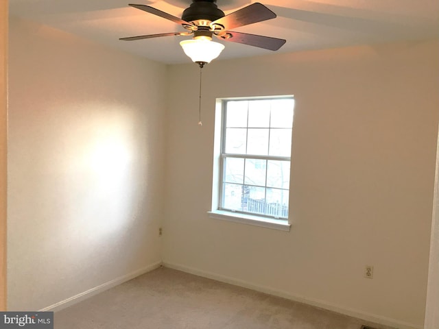 spare room featuring light colored carpet, a ceiling fan, and baseboards