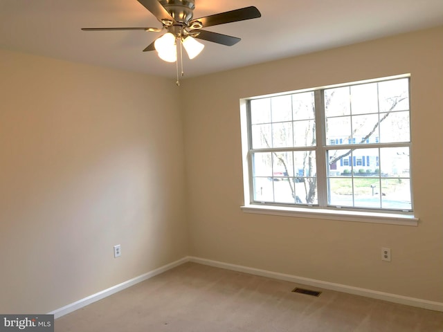 empty room with visible vents, light colored carpet, a ceiling fan, and baseboards