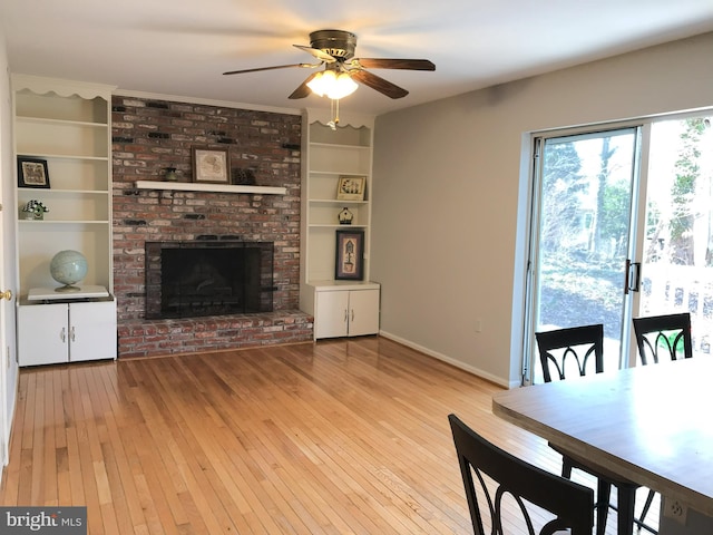 dining area featuring a ceiling fan, built in features, light wood-style floors, baseboards, and a brick fireplace