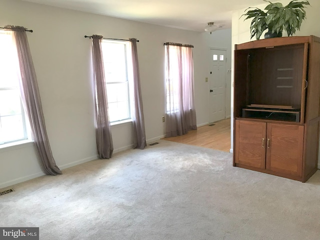 unfurnished living room with baseboards, visible vents, and light carpet