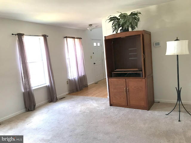 unfurnished living room with light carpet, baseboards, and a wealth of natural light