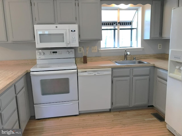 kitchen with white appliances, light countertops, light wood-style floors, and a sink