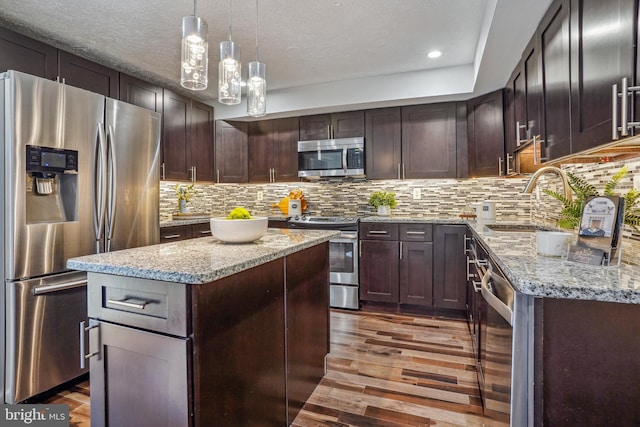 kitchen featuring a sink, wood finished floors, a center island, stainless steel appliances, and decorative backsplash