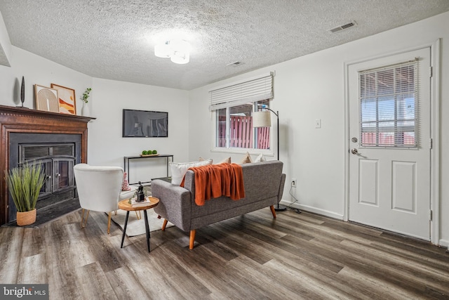 living area featuring wood finished floors, visible vents, baseboards, a fireplace, and a textured ceiling