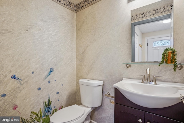 bathroom with toilet, vanity, and a textured wall