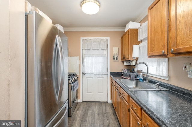 kitchen with brown cabinetry, ornamental molding, a sink, appliances with stainless steel finishes, and dark countertops