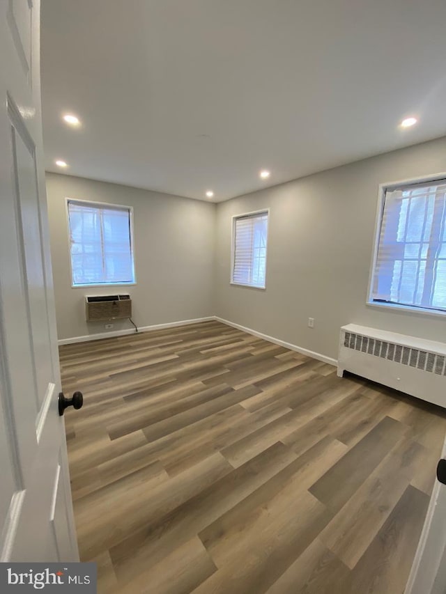 unfurnished room with radiator heating unit, wood finished floors, recessed lighting, and a wall mounted air conditioner