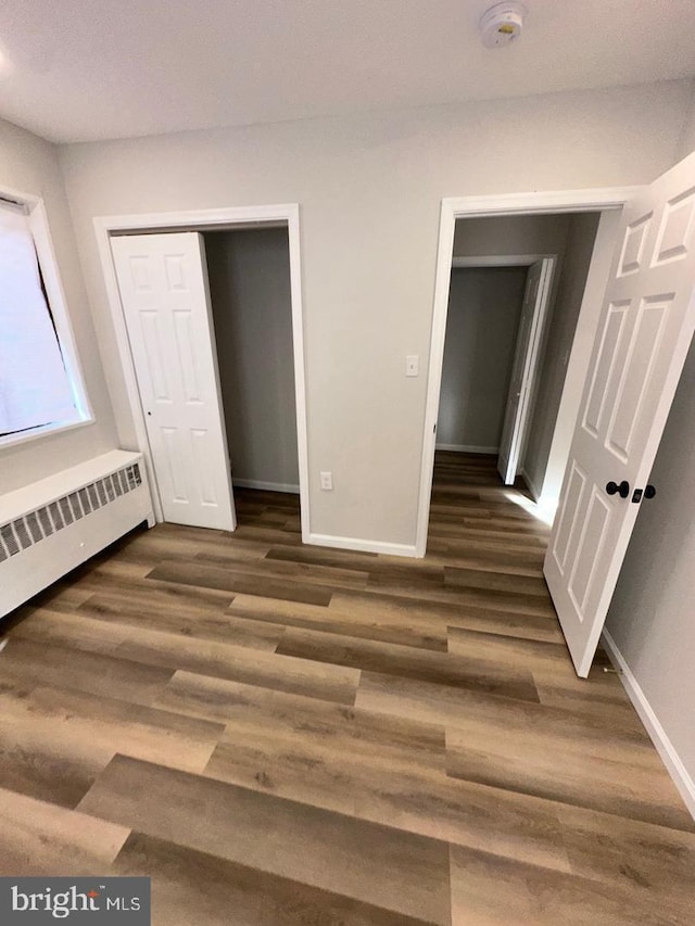 unfurnished bedroom with dark wood-style floors, radiator heating unit, and baseboards