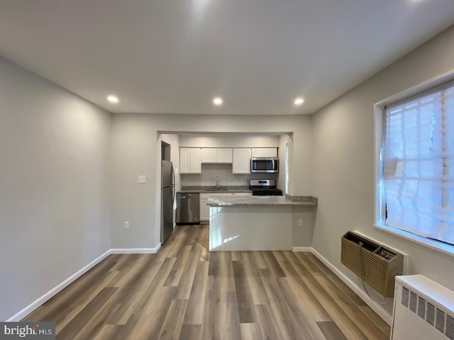 kitchen featuring an AC wall unit, radiator heating unit, stainless steel appliances, white cabinetry, and a sink