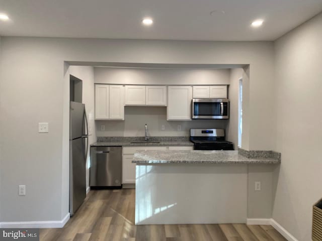 kitchen featuring a sink, appliances with stainless steel finishes, a peninsula, white cabinets, and light stone countertops